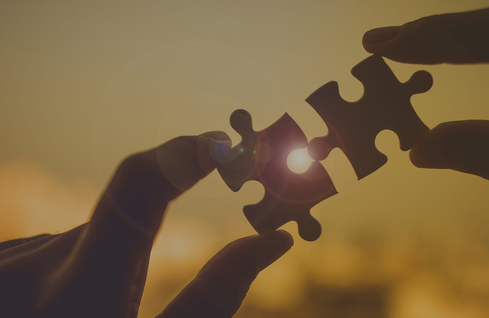 Close-up of two hands connecting puzzle pieces during a sunset