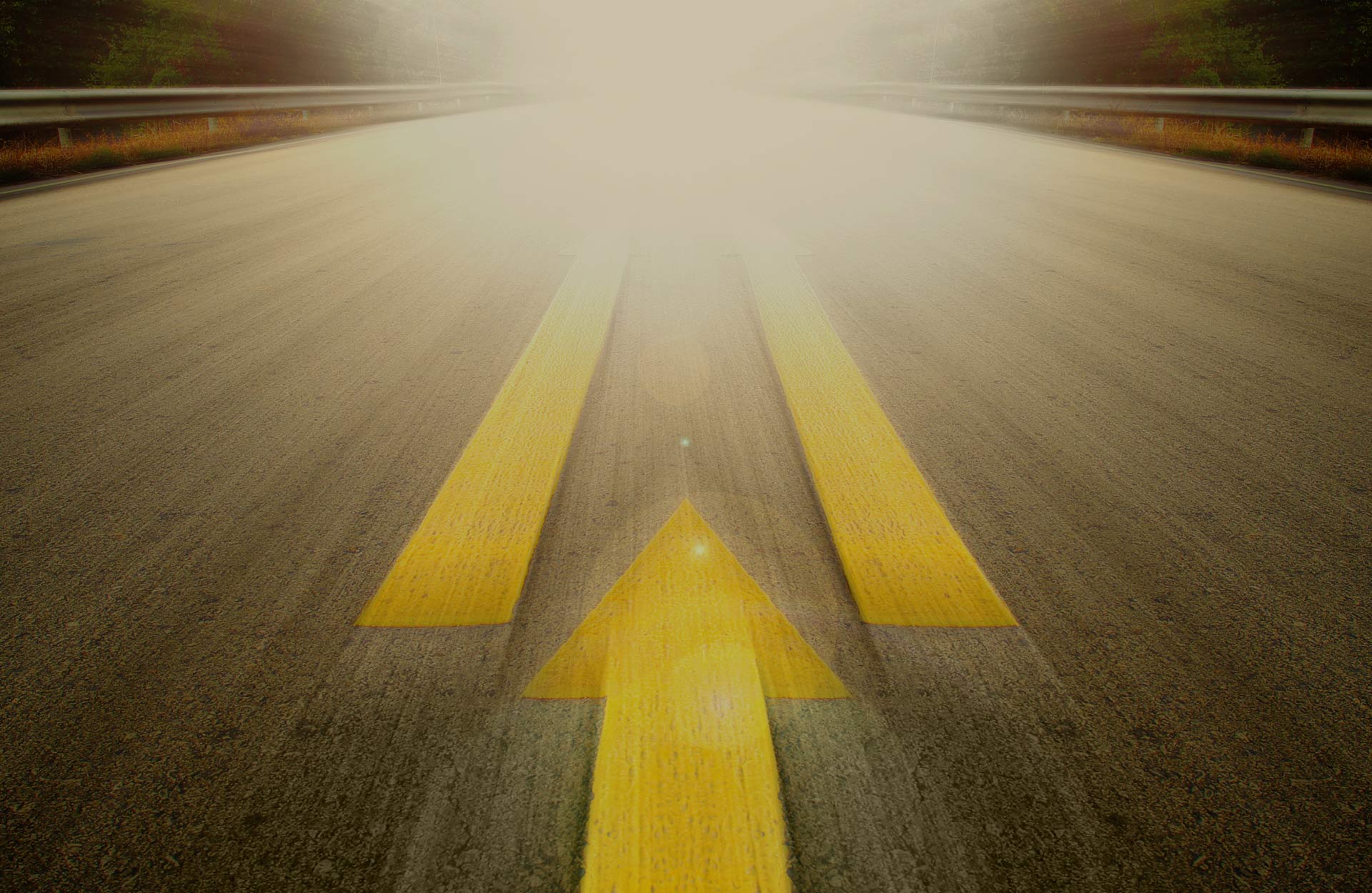 Close-up of an open road with a big yellow arrow pointing ahead